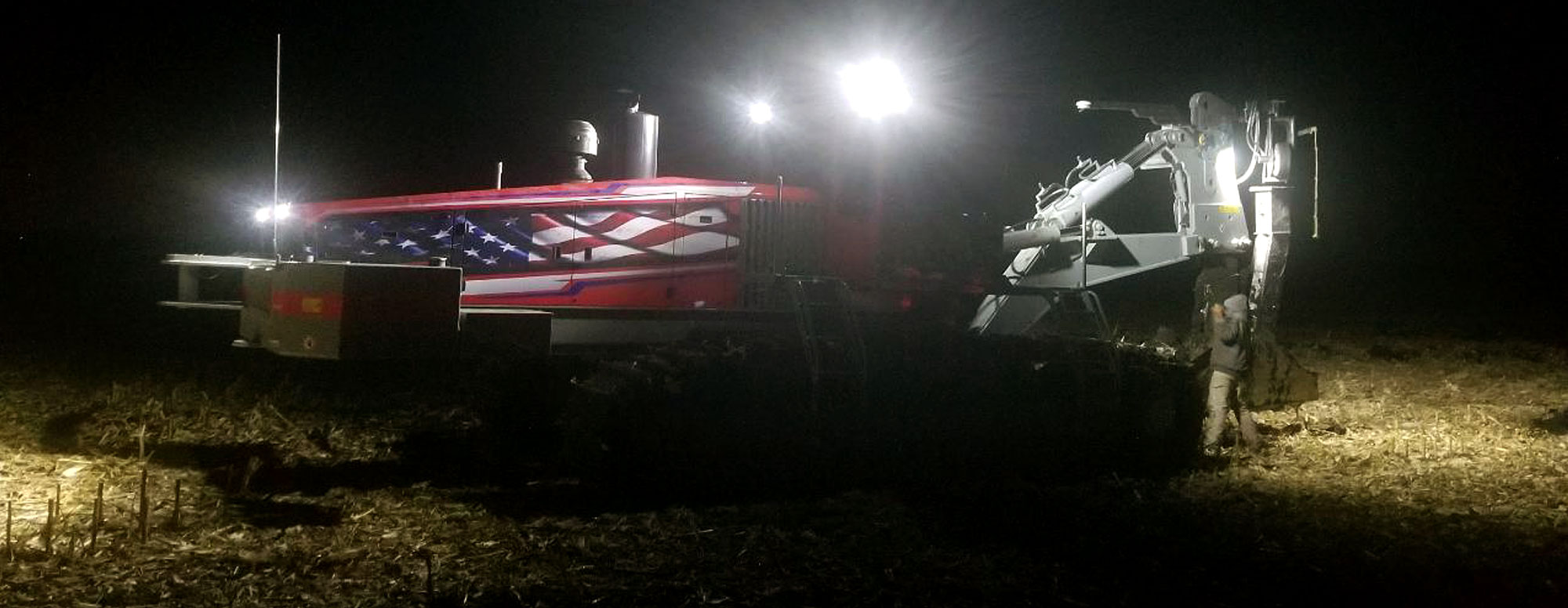 Dahle Enterprises' field tiling machine working in a field at night with its lights on